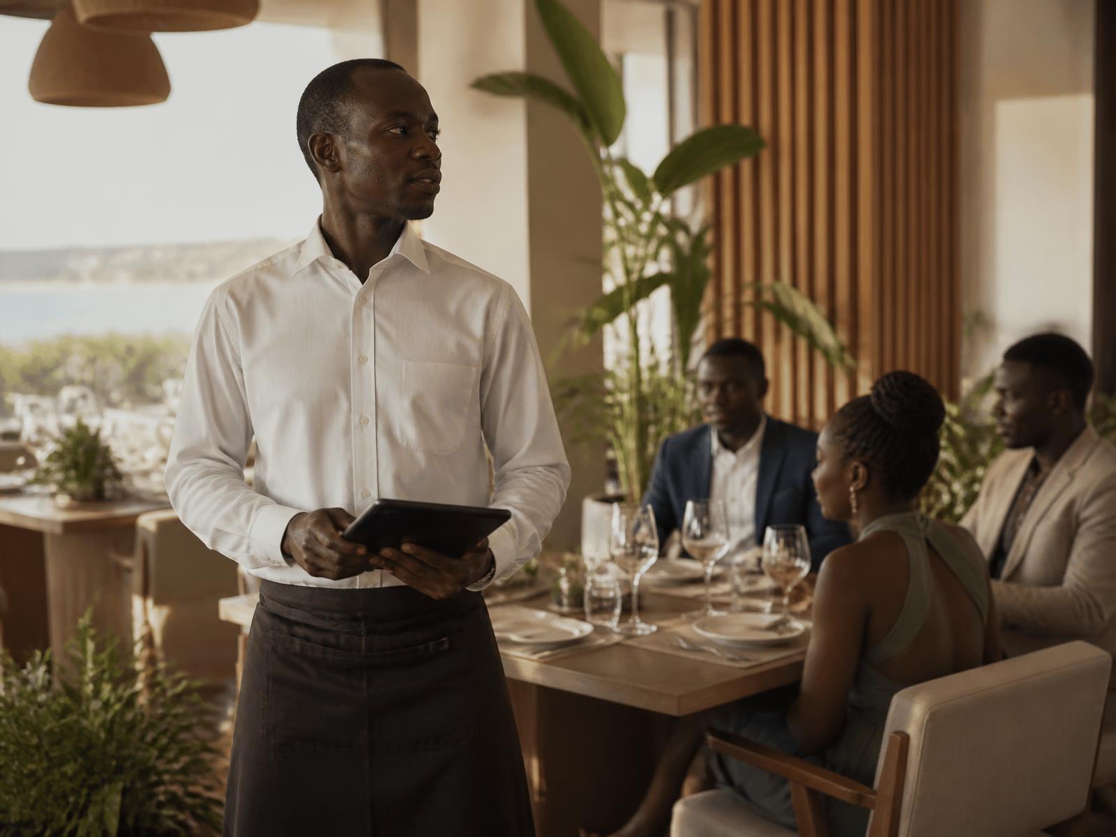 Serveur en salle d’un restaurant premium avec un terminal tablette pendant le service